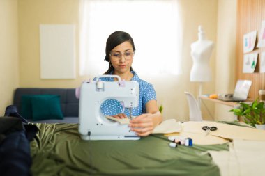 İspanyol moda tasarımcısı evden çalışıyor ve stüdyosunda elbise dikmek için dikiş makinesi kullanıyor.