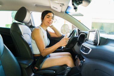 Stresli bir kadın yaz sıcak hava dalgası sırasında taşınabilir yelpaze kullanarak araba kullanıyor. Kırık klima yüzünden terliyor ve rahatsızlık duyuyor.