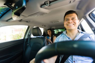Bir yolcu modern ulaşım hizmetlerini vurgulayarak arka koltukta mobil uygulama kullanırken, Rideshare sürücüsü güvenli bir şekilde arabayı sürüyor