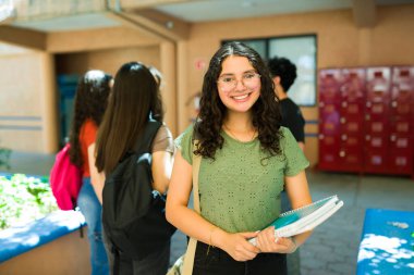 Not defteri taşıyan mutlu bir lise öğrencisinin portresi ve okul koridorunda arkadaşlarıyla gülümsemesi.