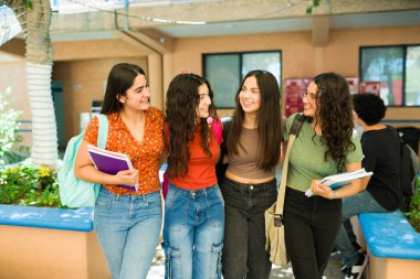 Teneffüste okul kampüsünde birlikte yürüyen neşeli çeşitli bayan öğrenciler, lise yaşam tarzlarının ve eğitimlerinin tadını çıkarıyorlar.