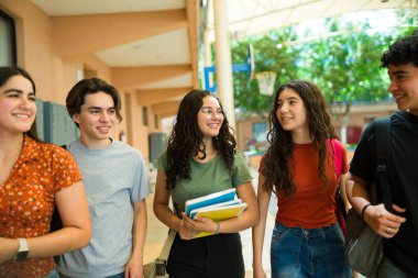 Koridorda sohbet ederken sırt çantaları ve not defterleri taşıyan bir grup Latin lise öğrencisi.