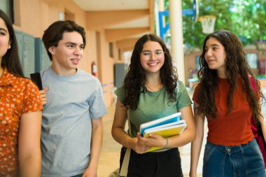 Okul koridorunda ders aralarında sırt çantası ve not defteri taşıyan mutlu lise öğrencileri.