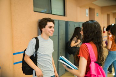 Gülümseyen gençler okul molasında dolapların yanındaki koridorda sohbet ediyorlar. Öğrenci olarak yaşam tarzlarının tadını çıkarıyorlar.