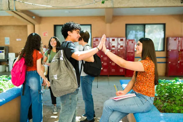 Mola sırasında okul koridorunda toplanıp arkadaşlığı ve gençliği kutlayan neşeli gençler beşlik çakıyor.