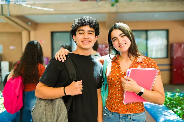 Okul koridorunda gülümseyen ve sırt çantaları ve not defterleri taşıyan iki mutlu lise öğrencisinin portresi