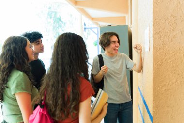 Notlarına bakan bir grup mutlu lise öğrencisi, bir okul duvarında başarıyı ve akademik başarıyı kutluyorlar.