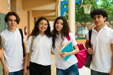 Beyaz üniformalı ve okul koridorunda sırt çantası taşıyan bir grup neşeli Latin lise öğrencisi.