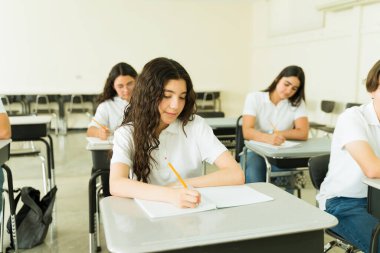 Üniforma giyen zeki lise öğrencileri ders sırasında not alıp ders çalışıyorlar.