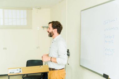 Lise öğretmeni, bir sınıf ortamında matematik kavramlarını beyaz tahtada açıklıyor ve öğrenciler için ilgi çekici bir öğrenme ortamı sağlıyor.