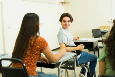 Neşeli erkek öğrenci lisede okurken arkasını dönüp bayan sınıf arkadaşıyla konuşuyor.