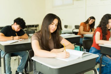 Lisedeki bir sınıfta sınava girerken not defterlerine yazan konsantre genç öğrenciler.