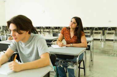 Konsantre olmuş lise öğrencisi notlar alıyor ve canlı bir sınıfta, öğrenme ve öğrenme dalmış bir ders sırasında yansıtıyor.