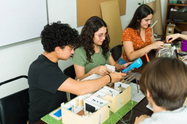 Kök sınıfı sırasında çoklu metre ve diğer araçları kullanarak bir elektronik projesinde işbirliği yapan bir grup lise öğrencisi
