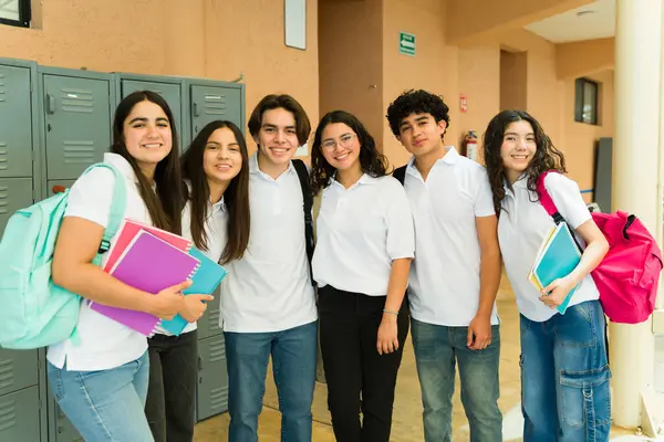 Okul koridorundaki dolapların yanında üniforma giyen çeşitli lise öğrencilerinin gülümsemesi.