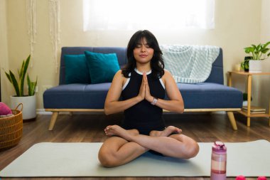 Huzurlu kadın yoga minderinde nilüfer pozu veriyor oturma odasında huzurlu meditasyondan keyif alıyor, sağlığını ve farkındalığını arttırıyor.