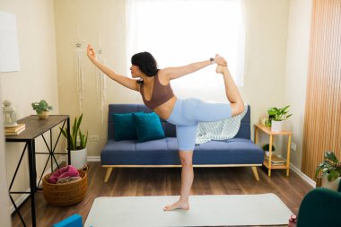 Dans lordu pozunu uygulayan aktif bir kadın, natarajasana olarak da bilinir, oturma odasında yoga minderinde denge ve esnekliği teşvik ediyor.