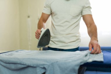 Adam ütü masasında gömlek ütülüyor, ev işlerini yapıyor ve düzenli bir ev ortamını koruyor.