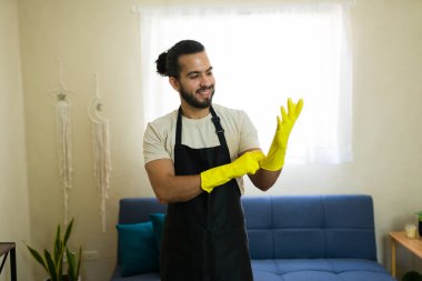 Sarı koruyucu eldiven ve siyah önlük giyen mutlu hizmetçi ev temizliğine hazırlanıyor.