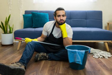 Modern oturma odasındaki ahşap zemini paspasladıktan sonra dinlenen hayal kırıklığına uğramış erkek hizmetçi ev işlerinden sıkılmış ve sıkılmış hissediyor.