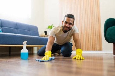 Sarı koruyucu eldivenler giyen bir adam apartmanın zeminini bez ve dezenfektan sprey şişesiyle temizliyor.