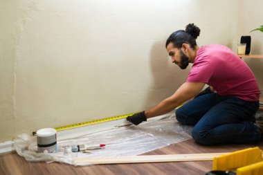 Tamirat ve onarım işleri için mezura kullanarak duvarın ölçüsünü alan tamirci.