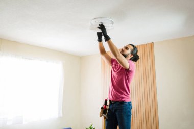 Modern bir evde tavan lambası montajında çalışan yetenekli bir tamirci, elektrik işi ve ev onarımı yapıyor.