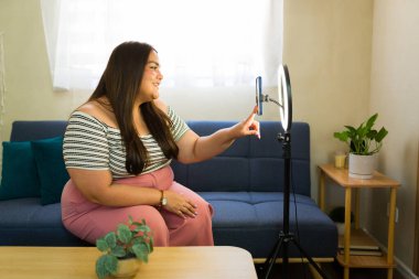 Mutlu ve boyutsal bir içerik oluşturucunun profil görünümü evde bir halka ışığı ve akıllı telefon kullanarak bir video blogu kaydediyor