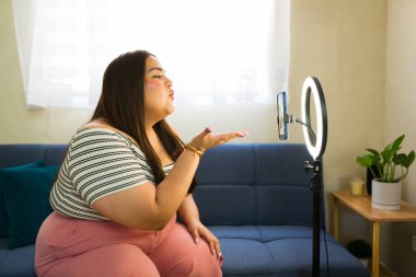 Oturma odasından canlı bir video blogu kaydederken ve güven ve pozitiflik yayarken büyük boy bir etki yaratan öpücükler yolluyor.