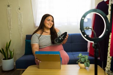 Mutlu genç bir kadın moda blogu için internetten yeni ayakkabıları inceliyor, kendini bir yüzük ışığıyla kaydediyor.