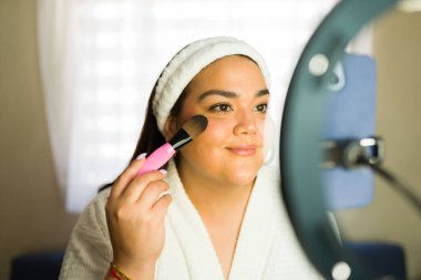 Latin içerik yaratıcısı, takipçileri için makyaj videosu çekerken bir fırçayla yüzüne temeli uyguluyor.