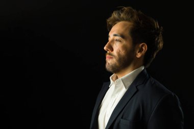 Siyah bir arka planda izole edilmiş, umut ve güvenle bakan bir iş adamının stüdyo portresi.