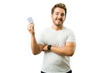 Stüdyoda beyaz bir arka planda dururken kredi kartı gösteren neşeli bir adamın portresi.