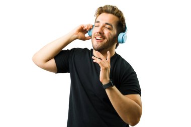 Gözleri kapalı, mavi kablosuz kulaklık kullanan, beyaz arka planda izole edilmiş, müzikten hoşlanan genç Latin bir adam.