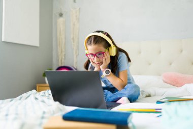 Çevrimiçi derslere katılan zeki ergen kız ve yatak odasında dizüstü bilgisayar kullanırken kulaklıkla öğretmenini dinliyor.