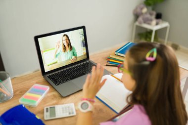 İlkokul öğrencisi evden öğrenirken öğretmenine videoda el sallıyor.