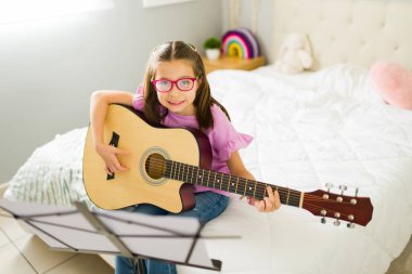 Mutlu küçük kız akustik gitar çalmayı öğreniyor ve yatak odasındaki müzik standından notalar okuyor.