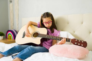 Yatak odasında rahat bir şekilde otururken gitar akoru çalmayı öğrenen tatlı ergen kız.