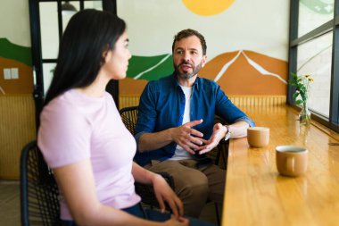 Kadın ve erkek, sıcak bir kafe masasında oturup neşeli bir sabah atmosferini kucaklarken kahve içerken keyifli bir sohbetin tadını çıkarıyorlar.