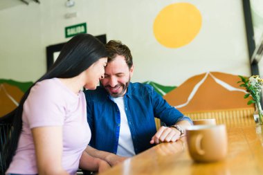 Latin çift bir kahve dükkanında romantik bir buluşmanın tadını çıkarıyor, gülümsüyor ve alınlarına dokunuyor, birlikte sevgi ve mutluluk yayıyor.