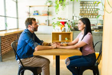 İspanyol çift romantik bir buluşmadan zevk alıyor, el ele tutuşup sohbet ediyorlar ve sıcak bir kafede kahve içiyorlar.