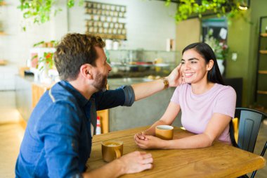 Romantik çift el ele tutuşuyor ve kafe masasında kahve içerken hassas bir an yaşıyor.