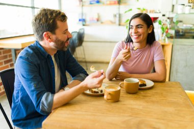 Neşeli bir çift, hoş bir kafede romantik bir buluşmanın tadını çıkarıyor. Pastanın tadını çıkarıyor, kahkahalarını yudumluyor ve gülümsüyor.