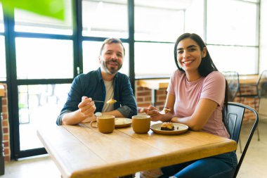 Gülümseyen bir çift, şık, modern bir kafede neşe dolu bir randevuyu paylaşırken lezzetli pastadan ve kahveden zevk alıyor.