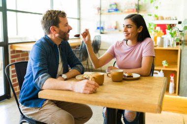 Latin bir kadın bir kafede romantik bir buluşmanın tadını çıkarırken erkek arkadaşıyla bir parça kek yiyor.