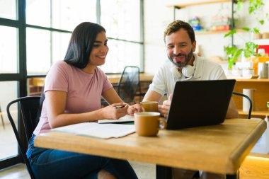 Kahve dükkanında dizüstü bilgisayarla gülümseyen ve işbirliği yapan iki kişi kahve ve uzaktan çalışmanın keyfini çıkarıyorlar.