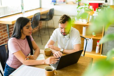 İki serbest çalışan, bir kafede dizüstü bilgisayar üzerinde çalışırken bir projeyi tartışıyorlar, kahve ve verimli bir çalışma ortamının keyfini çıkarıyorlar.