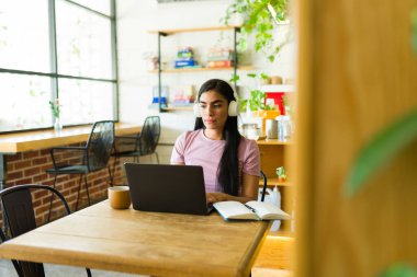 Kafede dizüstü bilgisayarla çalışan, kulaklık takan ve not alan, uzak çalışma ortamının tadını çıkaran serbest çalışan biri.