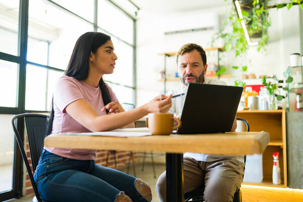 Мужчина и женщина участвуют в обсуждении проекта, сидя в кафе, используя ноутбук и записывая заметки
