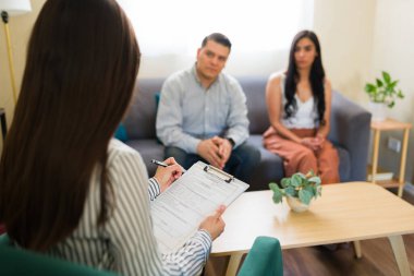 Latin çift terapi seansında profesyonel psikolojik destek alıyor. Ruh sağlığı uzmanı panoya not alıyor.